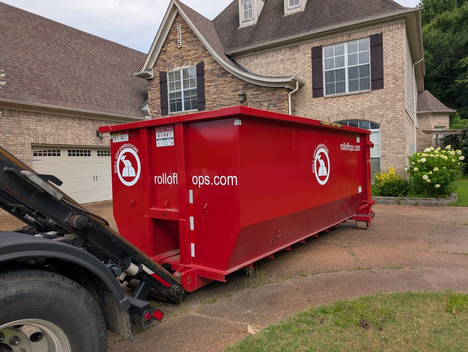 Roll Off Operations truck placing a red 20-yard dumpster on a residential driveway