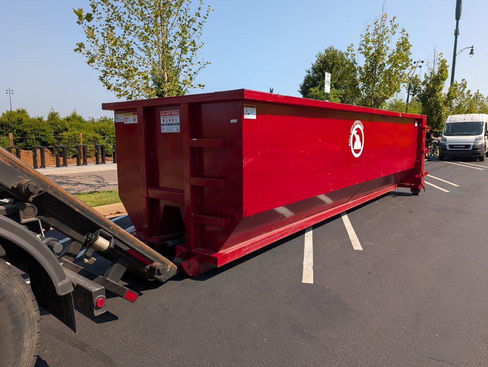 Red 30-yard Roll Off Operations dumpster being placed in a paved parking lot